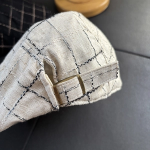 Detail of adjustable bronze metal buckle on checkered linen blend newsboy flat cap