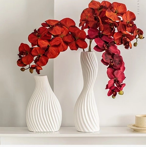 Close-up of white ceramic vases with twisted texture and bright artificial orchids