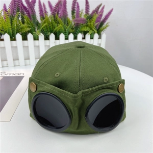 Detail of army green baseball cap featuring black aviator goggles and bronze snap buttons
