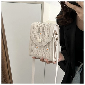 Detail of straw woven crossbody bag featuring daisy embroidery and slim strap