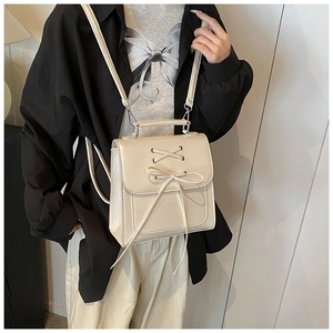 Detail of a beige cream PU leather bag featuring a crossbody strap and bow tie decoration