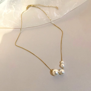 Détail du collier en chaîne dorée avec quatre perles blanches dégradées sur tissu beige