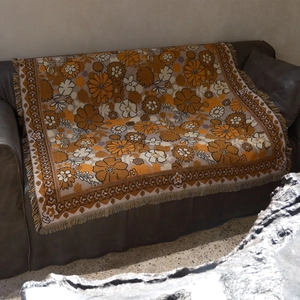 Close-up of vintage floral woven throw blanket with orange tassels on leather sofa