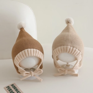 Detail of baby knitted elf hat with pom-pom and earflaps in brown and beige colors