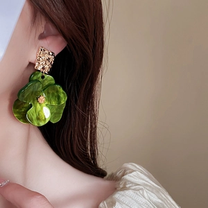 Close-up of green flower earring with golden textured metal plate on female model