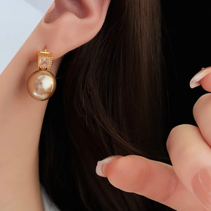 Detailed view of square gold earrings with crystals and hanging golden pearls on model