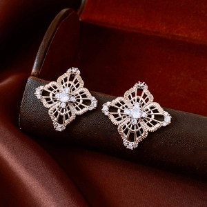 Detail of rose gold geometric earrings with white zircon on dark leather and silk background