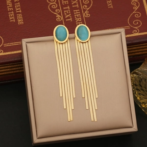 Elegant gold tassel earrings with oval blue cat eye stones on a beige jewelry cushion