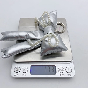 Silver bow keychain with pearls and metal texture on scales showing weight of 17.3g