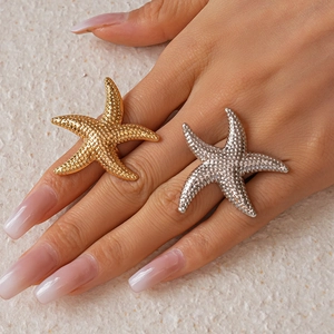 Macro detail of starfish shaped gold and silver rings with beaded texture on a model's hand