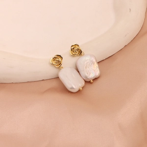 Detailed view of baroque pearl earrings with golden floral hooks on pink silk fabric