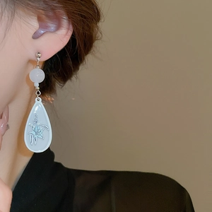 Detail of white teardrop earring with floral pattern and translucent bead on silver stud