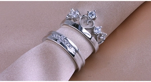 Macro shot of silver crown and cross couple rings with diamonds on silk background