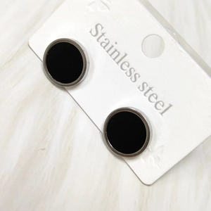 Macro detail of black stainless steel round stud earrings on a white jewelry display card