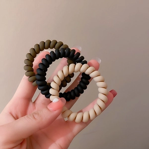 Three-piece matte spiral hair ties in brown, black and beige held in hand