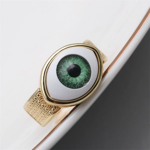 Detail of a gold-plated copper ring with green eye decor and grid-textured band