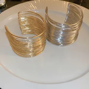 Exaggerated layered hollow open cuff bracelets in gold and silver finish on white ceramic