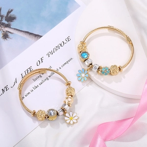 Detail of gold woven bracelets featuring white and blue daisy charms with enamel beads