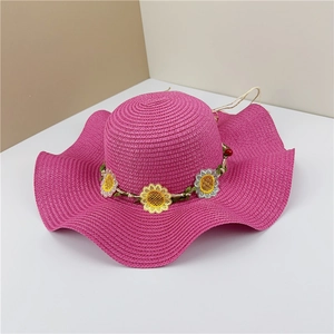 Détail d'un chapeau de paille rose rouge avec bord ondulé et fleurs de marguerites