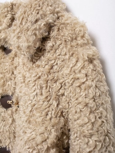 Detailed view of curly fleece texture with brown leather patch and gold metal buckle