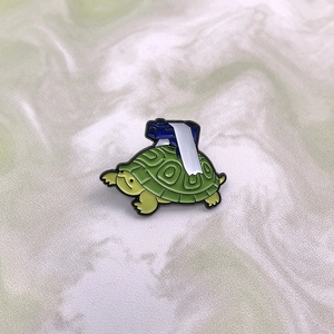 Creative green turtle enamel pin with camera accessory, shown from a 45-degree angle