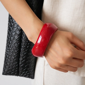 Close-up of wide red acrylic geometric bangle worn with white linen and black bag