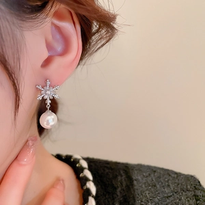 Macro detail of snowflake zircon earrings with a hanging pearl on a model's ear