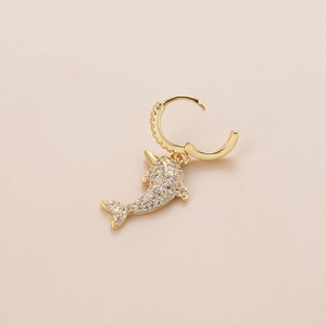 Detailed view of a gold dolphin pendant earring with pave cubic zirconia on beige surface