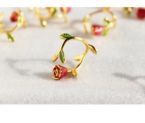 Macro shot of handcrafted gold ring with red enamel rose and green leaf details
