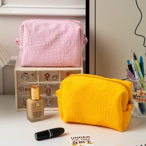 Detail view of pink and yellow pleated cosmetic bags on a makeup desk.