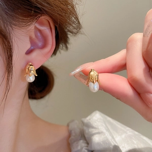 Elegant gold flower earrings with white teardrop pearl drop shown on model's ear