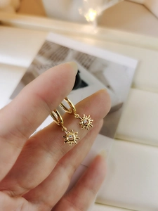 Macro shot of gold sun earrings with clear zircon center held between fingers