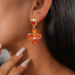 Close-up of golden clover earrings with amber resin stones on a model's ear