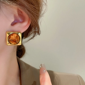 Close-up of square golden earrings with amber resin inlay worn on a model's ear