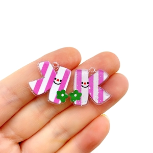 Close-up of pink striped acrylic letter charm with small green flower and smiley face