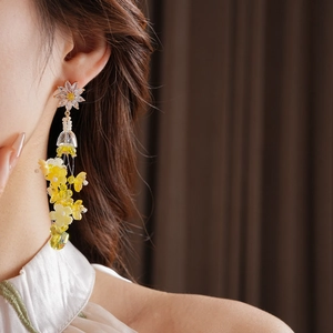 Gros plan de boucles d'oreilles pendantes fleurs jaunes et cristaux portées par un mannequin