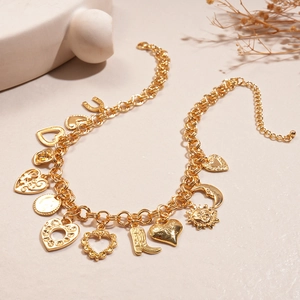 Detail of gold chain necklace with celestial sun moon and heart pendants on neutral background