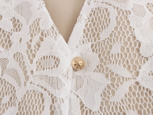 Detail shot of a white lace garment featuring a delicate golden hollowed-out button closure