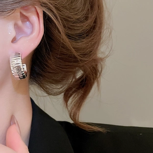 Close-up of silver C-shaped hoop earrings with ridged texture on model ear