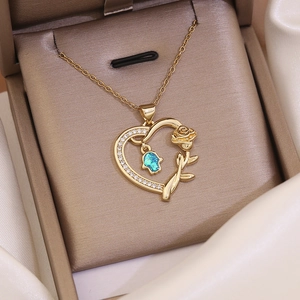 Detail of 18K gold heart pendant necklace with blue Fatima hand and rose charm in jewelry box