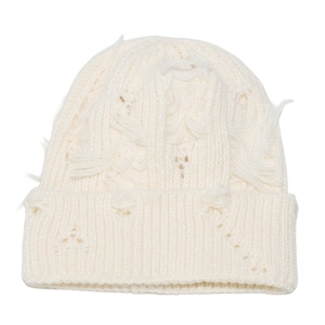 Detail of distressed knit beanie featuring chunky cream yarn with ripped holes and tassels