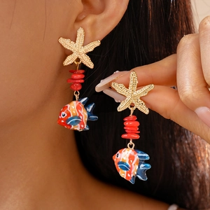Detailed shot of starfish and tropical fish dangle earrings worn for beach vacations