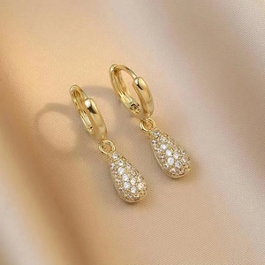 Macro shot of gold teardrop earrings with pavé crystals on a luxury champagne satin background