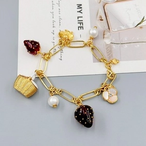 Close-up of charm bracelet with red strawberry, white pearl, and golden basket details