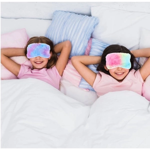 Detailed view of two children wearing colorful plush sleep masks on a cozy white bed