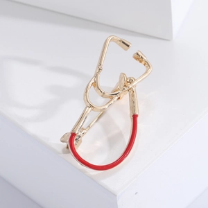 Elegant gold and red stethoscope brooch displayed on a white geometric pedestal stand