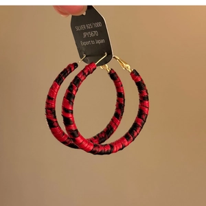 Détail de créoles tissées à motif léopard rouge et noir avec étiquettes en argent