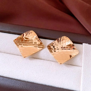 Macro shot of gold-plated square stud earrings with wave texture in a jewelry box