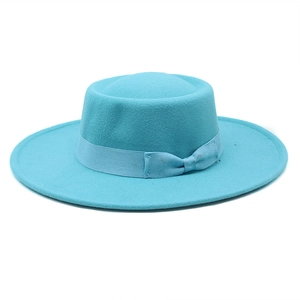 Detail of light blue flat top wool hat with matching ribbon and bow on plain background