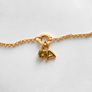 Macro view of a gold stainless steel bracelet with a yellow gemstone and letter A pendant.